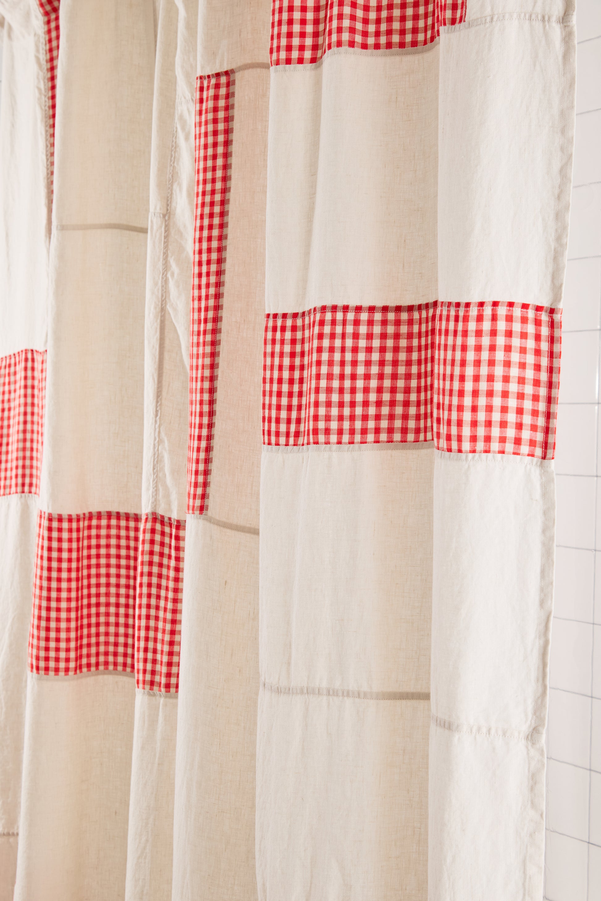 Shower curtain with red and white checkered pattern on a tiled bathroom wall.