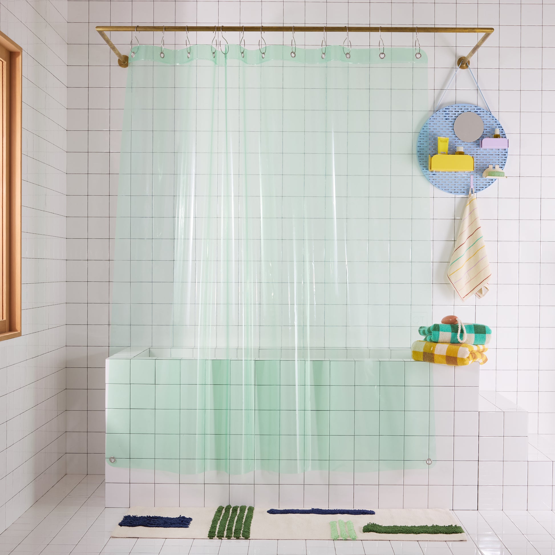 Bathroom with a clear green shower curtain, colorful bath organizer, and towels.
