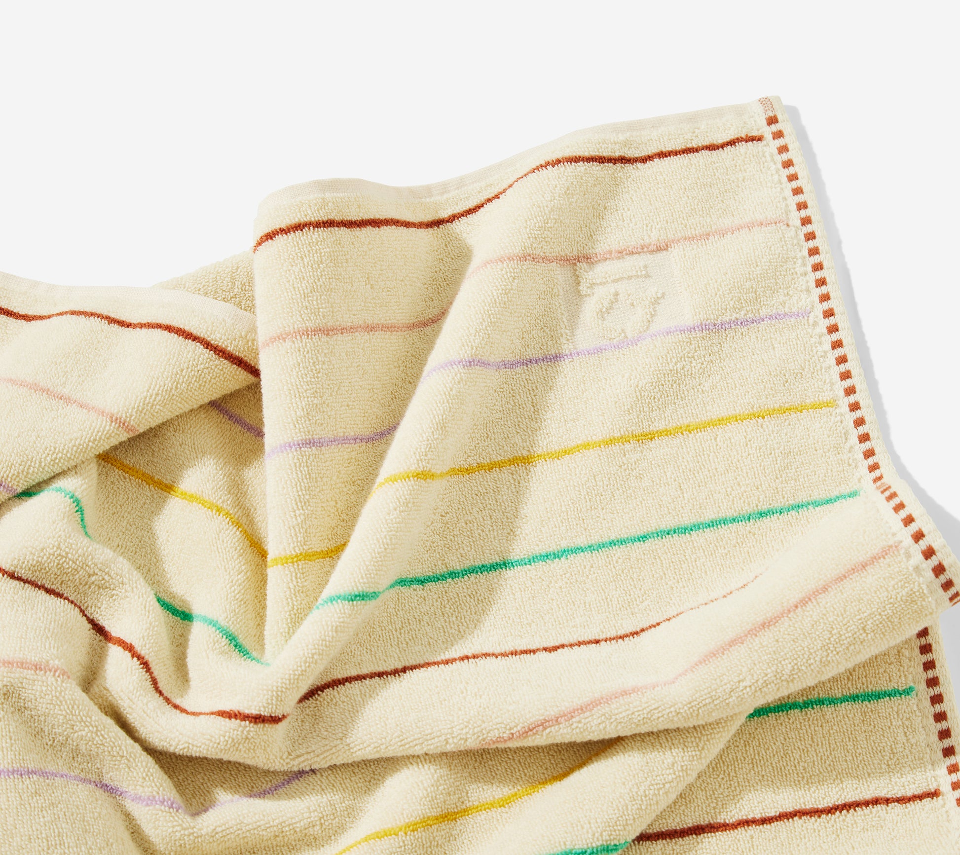 Corner detail of prism bath towel with multi-color pin stripes and an embossed QT logo.