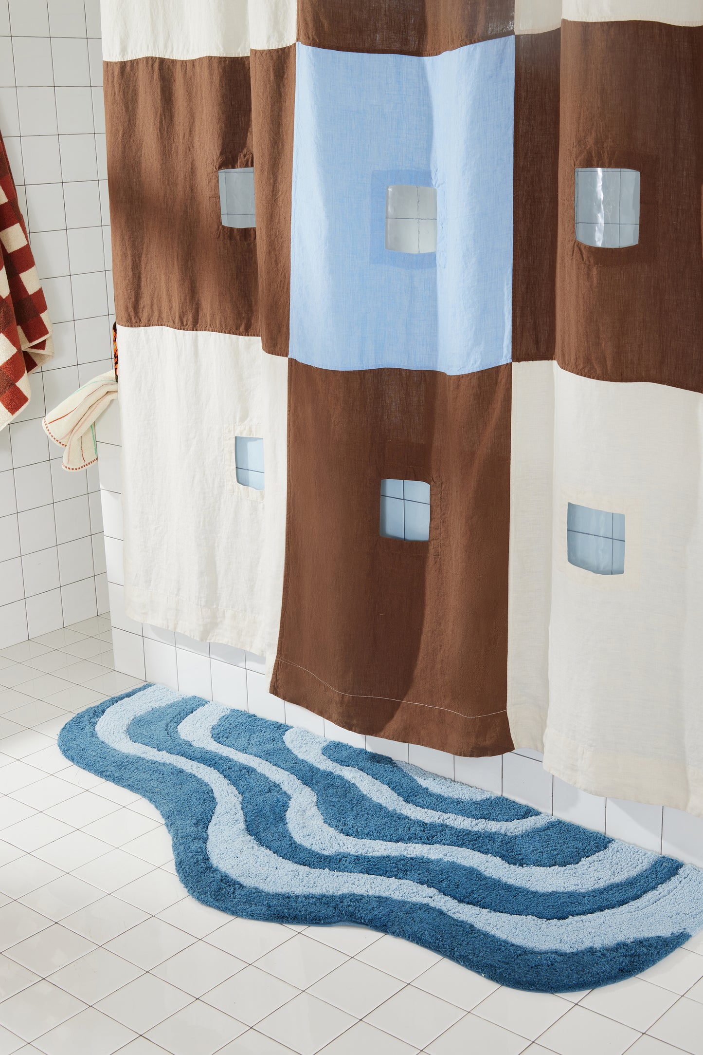 dark and light blue wavy bath runner on white tiled floor next to brown and blue shower curtain. 