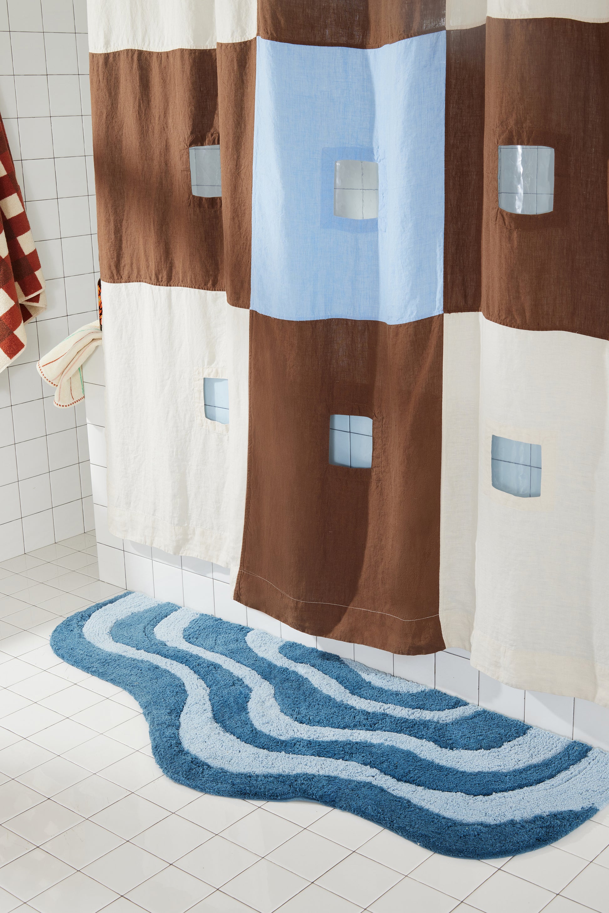 dark and light blue wavy bath runner on white tiled floor next to brown and blue shower curtain. 