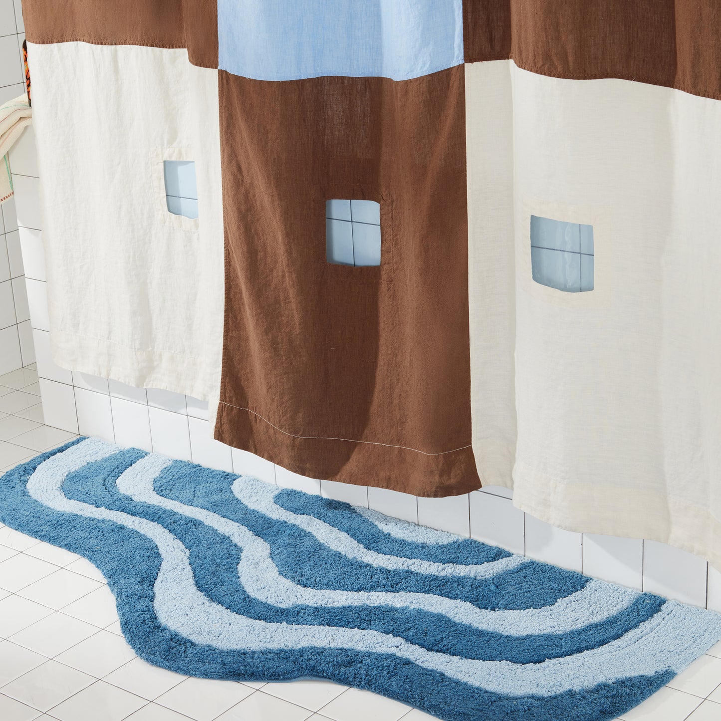 dark and light blue wavy bath runner on white tiled floor next to brown and blue shower curtain. 