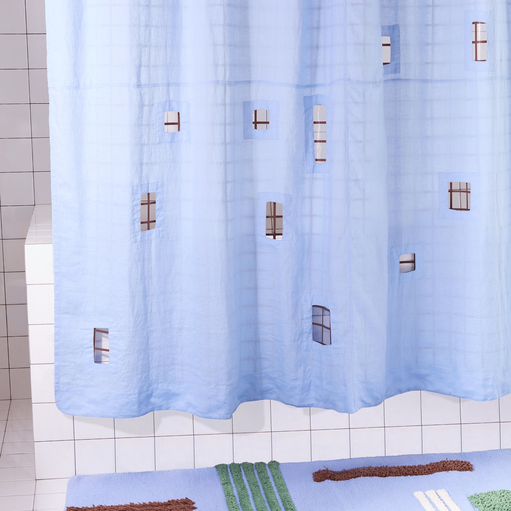 light blue shower curtain with cut outs in a white tiled bathroom and a blue pattern rug. 